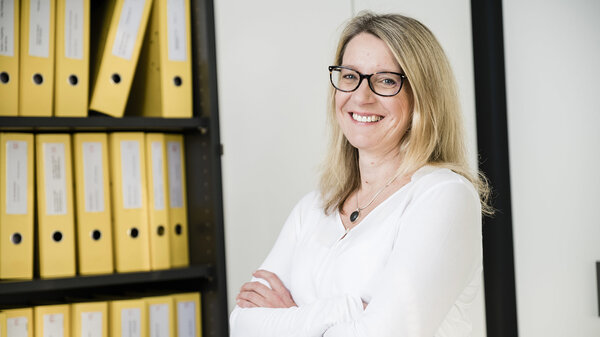 Steuerfachangestellte steht lächelnd vor einem Aktenschrank
