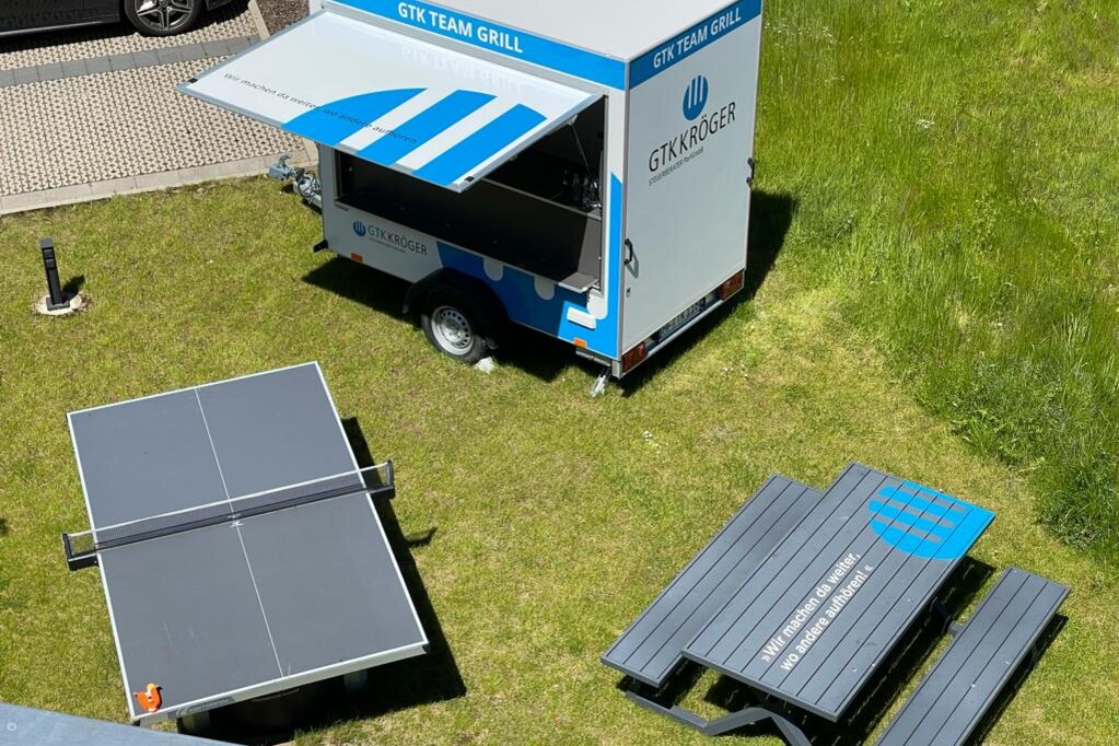 Blick von von aus dem Bürogebäude von GTK Kröger Steuerberater auf den Team-Grill-Wagen, Outdoor-Tischtennisplatte und Tisch mit Sitzbänken