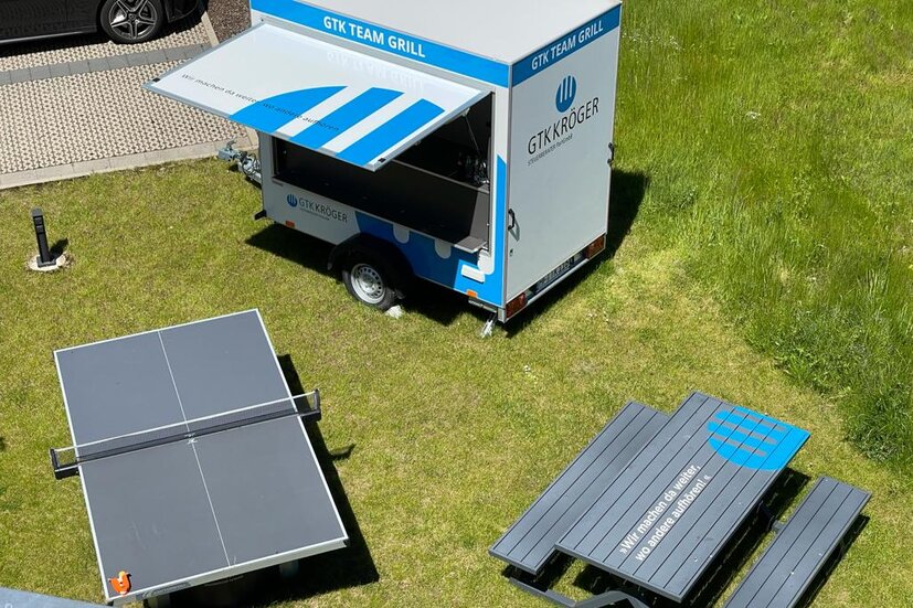 Blick von von aus dem Bürogebäude von GTK Kröger Steuerberater auf den Team-Grill-Wagen, Outdoor-Tischtennisplatte und Tisch mit Sitzbänken